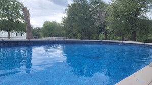 A swimming pool with clear blue water, surrounded by trees and a white building with a decorative pool edge. - The Perfect Getaway (Elgin)