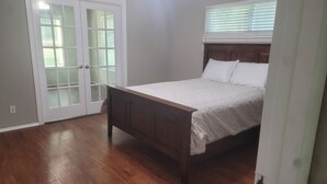 A bedroom with a wooden bed, a white door with glass panels, and a window with blinds. - The Perfect Getaway (Elgin)