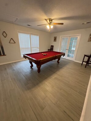 A room with a pool table, a ceiling fan, and a door with glass panels.