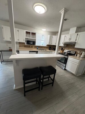A modern kitchen with white cabinetry, a central island with stools, and a built-in oven.