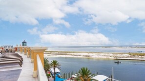 A waterfront hotel with a balcony overlooking a calm sea, a small boat on the water, and a clear sky.