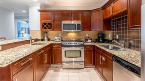 A kitchen with wooden cabinets, granite countertops, stainless steel appliances, and a tiled backsplash.
