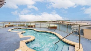 A pool area with a curved design, surrounded by a glass barrier, and a view of the beach in the background.