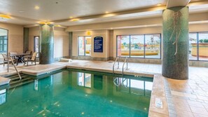 An indoor swimming pool with clear water, surrounded by stone pillars, and a seating area with chairs. - Destin | Group Emerald Coast Getaway | Pool + Beach | 4BR Sleeps 10 (Destin)