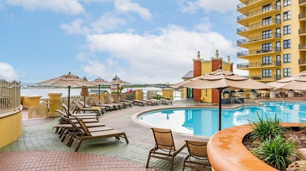 A pool area with lounge chairs and umbrellas, a pool, and a building with balconies.