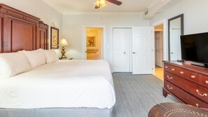 A hotel room with a large bed, a wooden dresser, a television, and a ceiling fan. - Destin | Group Emerald Coast Getaway | Pool + Beach | 4BR Sleeps 10 (Destin)