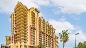 A multi-story hotel with balconies, a flag, and palm trees.