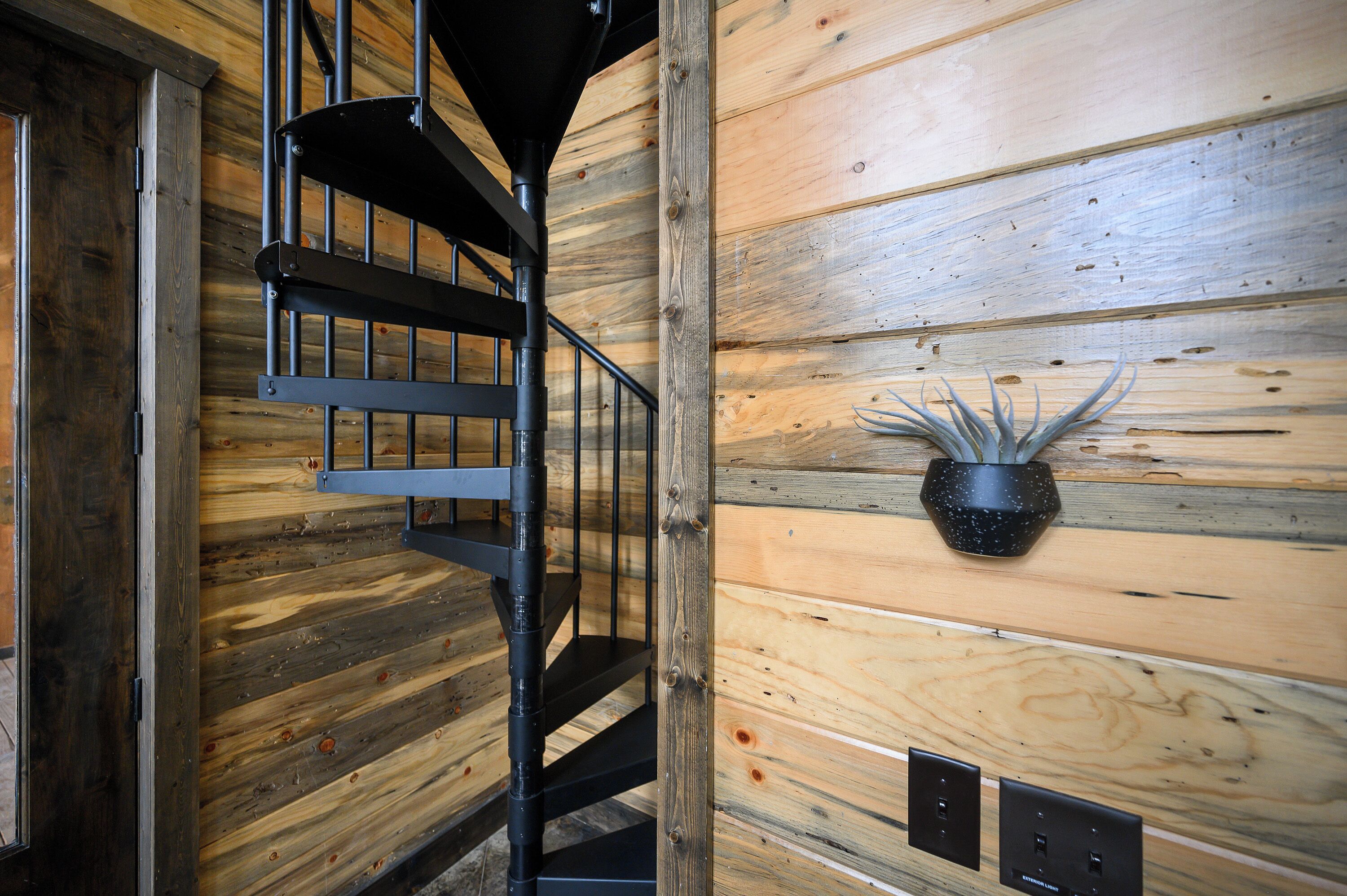 A spiral staircase with a black metal railing against a wooden wall.