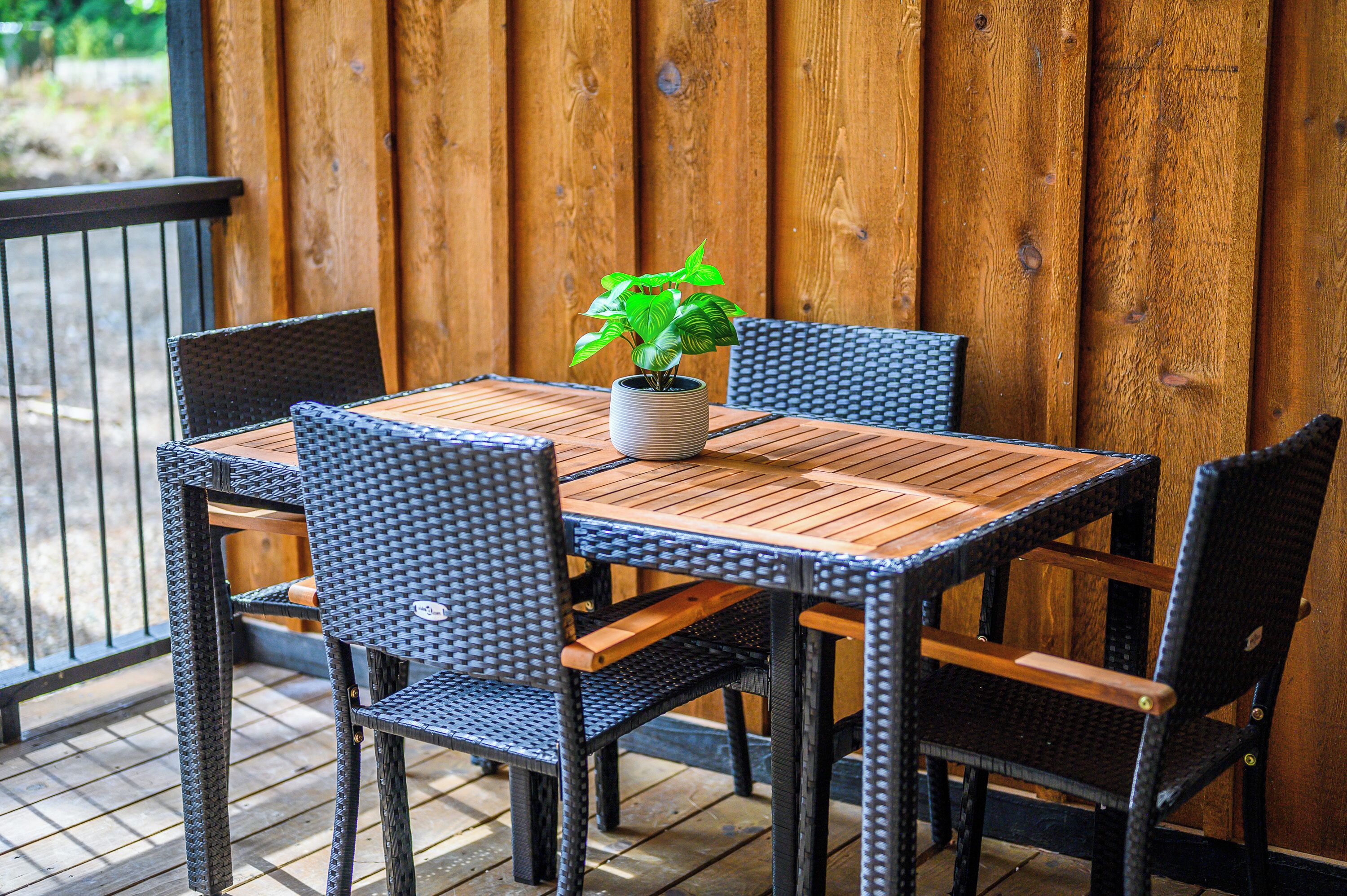 Una mesa de madera con cuatro sillas, una planta en maceta y una cerca de madera al fondo.