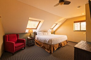 Een hotelkamer met een bed, een rode fauteuil, twee nachtkastjes met lampen en een plafondventilator.