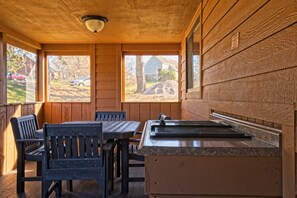 A covered outdoor seating area with a table and chairs, a countertop with a sink, and large windows offering views of the surrounding area.