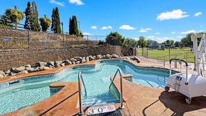 A swimming pool with a 3-foot depth marker, surrounded by a brick wall, a grassy area, and trees. - Wisconsin Dells | Pool & Waterpark Access | 2BR Villa (Wisonsin Dells)
