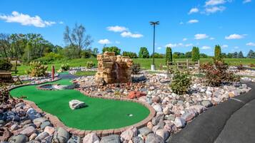 Un parcours de minigolf avec un tapis vert pour les putts, un obstacle constitué d’une formation rocheuse et une clôture en bois en arrière-plan.