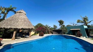 En swimmingpool med en bindingsværksbygning i nærheden, omgivet af palmer og frodig vegetation.