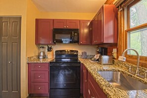 A kitchen with a granite countertop, stainless steel sink, and red cabinets.