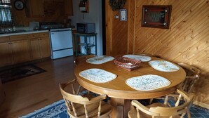 Une table à manger en bois, avec des sets de table et des chaises, une cuisine en arrière-plan et un panneau encadré accroché au mur.