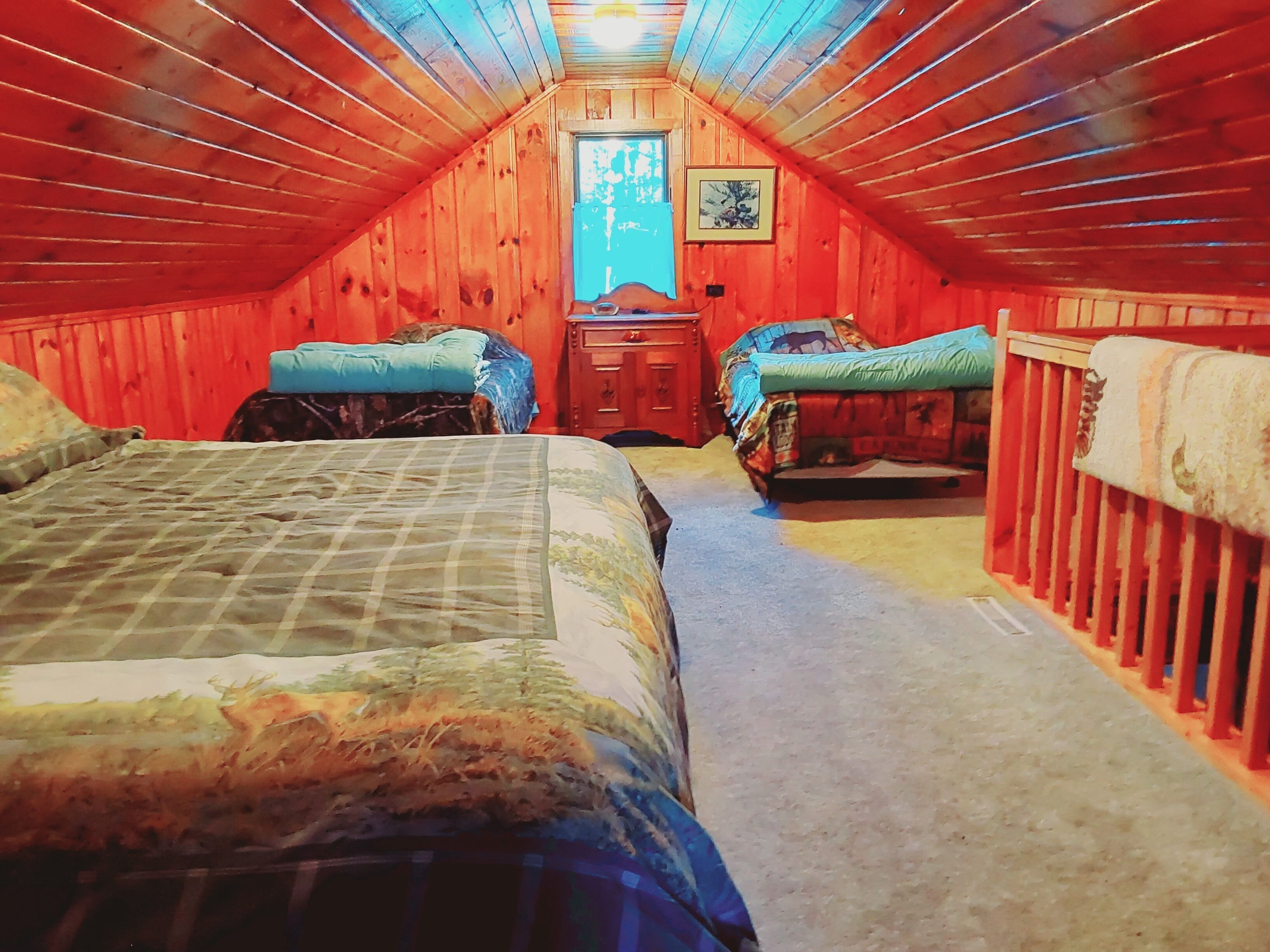 An attic bedroom with two beds, a wooden ceiling, and a window with a view.