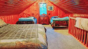 An attic bedroom with two beds, a wooden ceiling, and a window with a view.