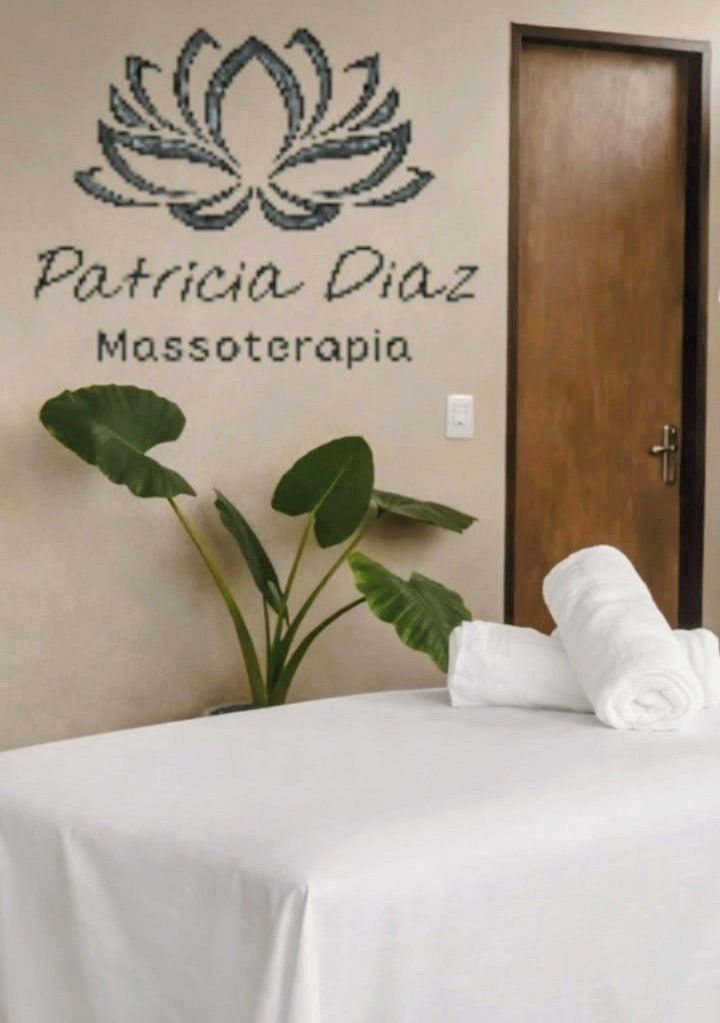 A room with a bed, a wall-mounted sign reading 'Patricia Diaz Massoterapia,' and a potted plant.