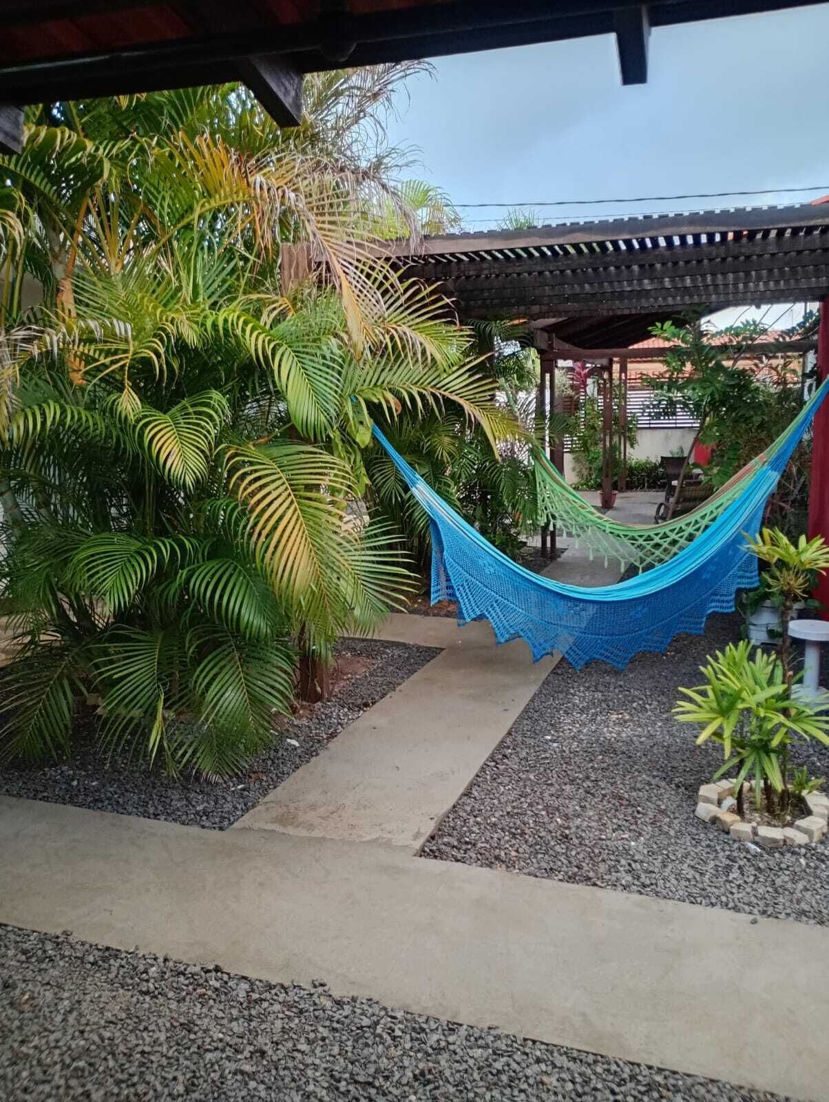 Una hamaca bajo una pérgola con plantas tropicales y un sendero de grava.