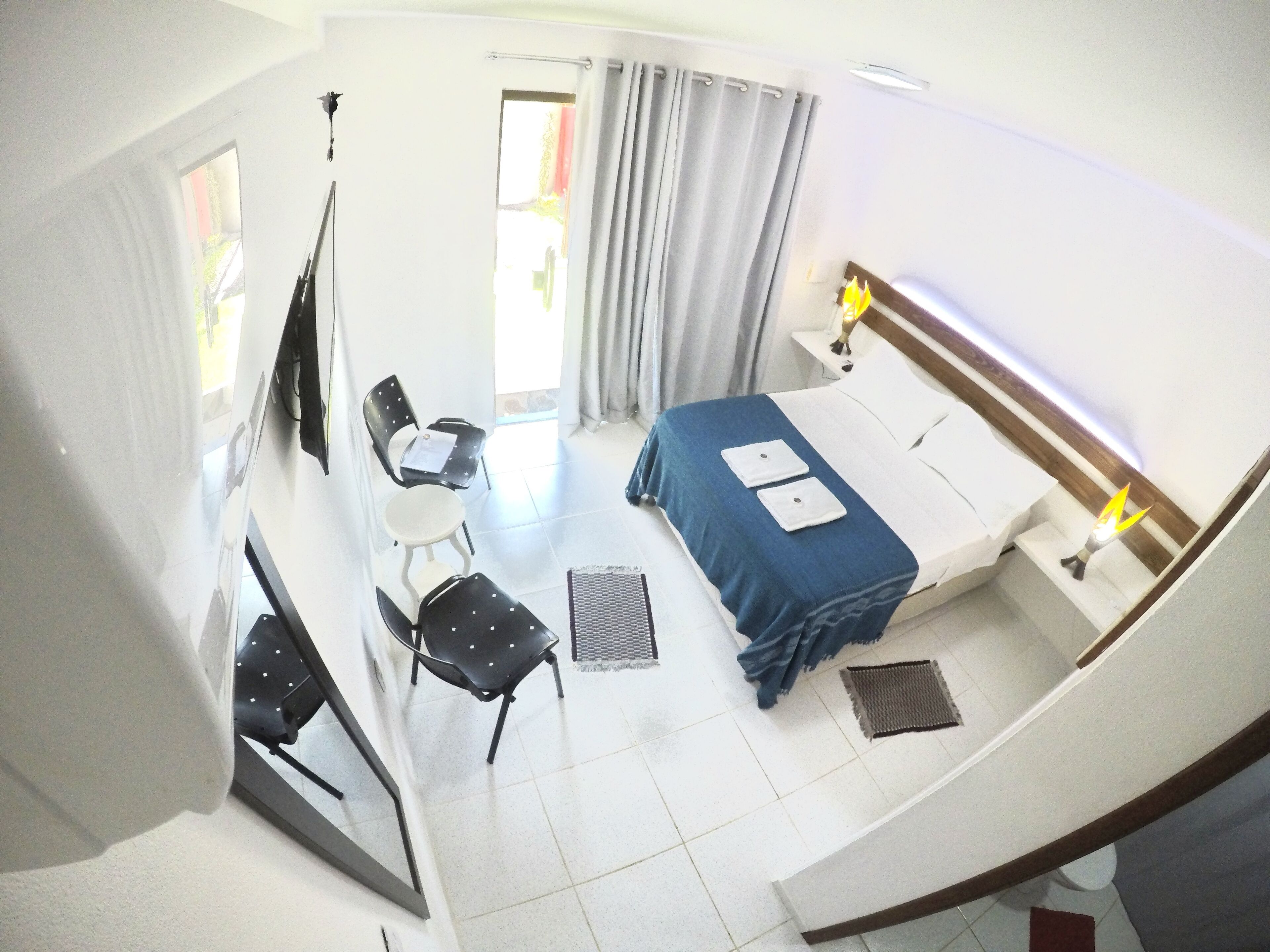 Habitación de hotel con cama, dos sillas, una mesita, un espejo y ventana con cortinas.