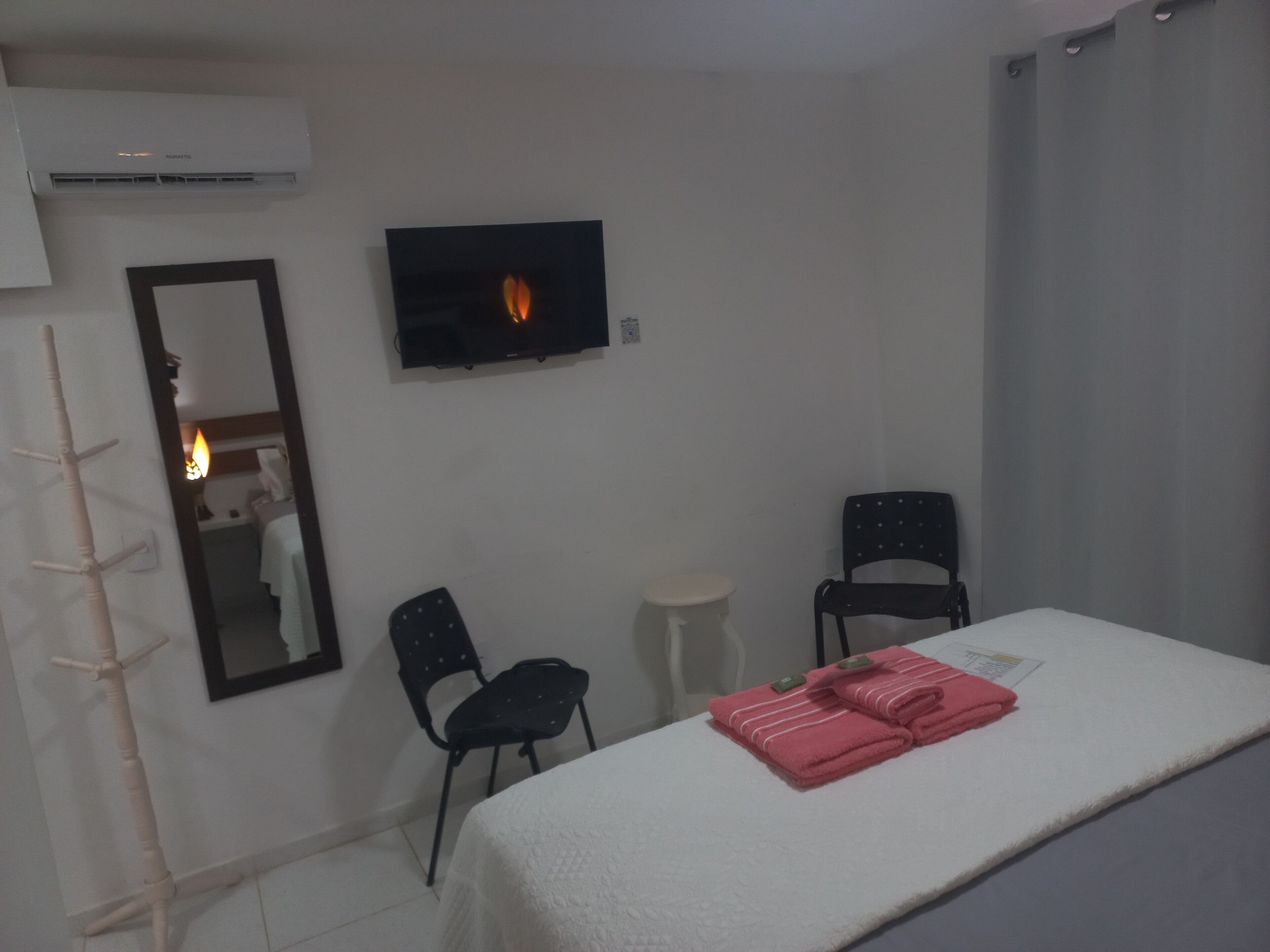 Ein Zimmer mit einem Bett, zwei Stühlen, einem kleinen Tisch, einem Fernseher und einem Spiegel.