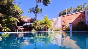 Ein klares, blaues Schwimmbecken, umgeben von üppiger Vegetation und einer Ziegelmauer.