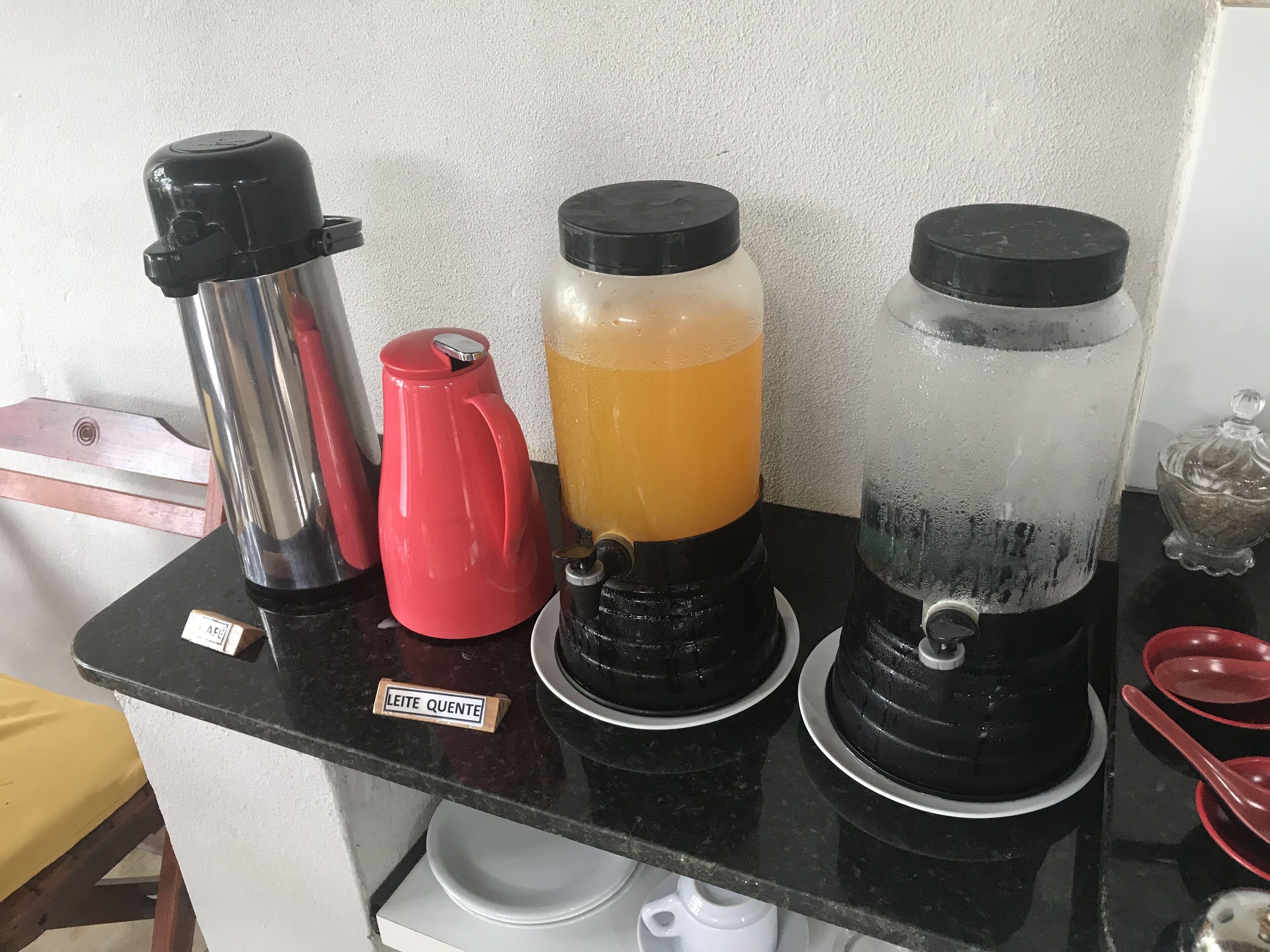 Een keukentoog met drie drankdispensers, een rode waterkoker en een bordje met de tekst 'Leite Quente'.