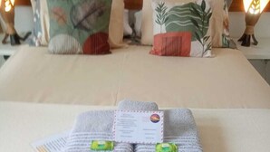 A neatly made bed with towels and a card, pillows with leaf patterns, and a wooden headboard. - Ayre Gostoso Pousada (São Miguel do Gostoso)