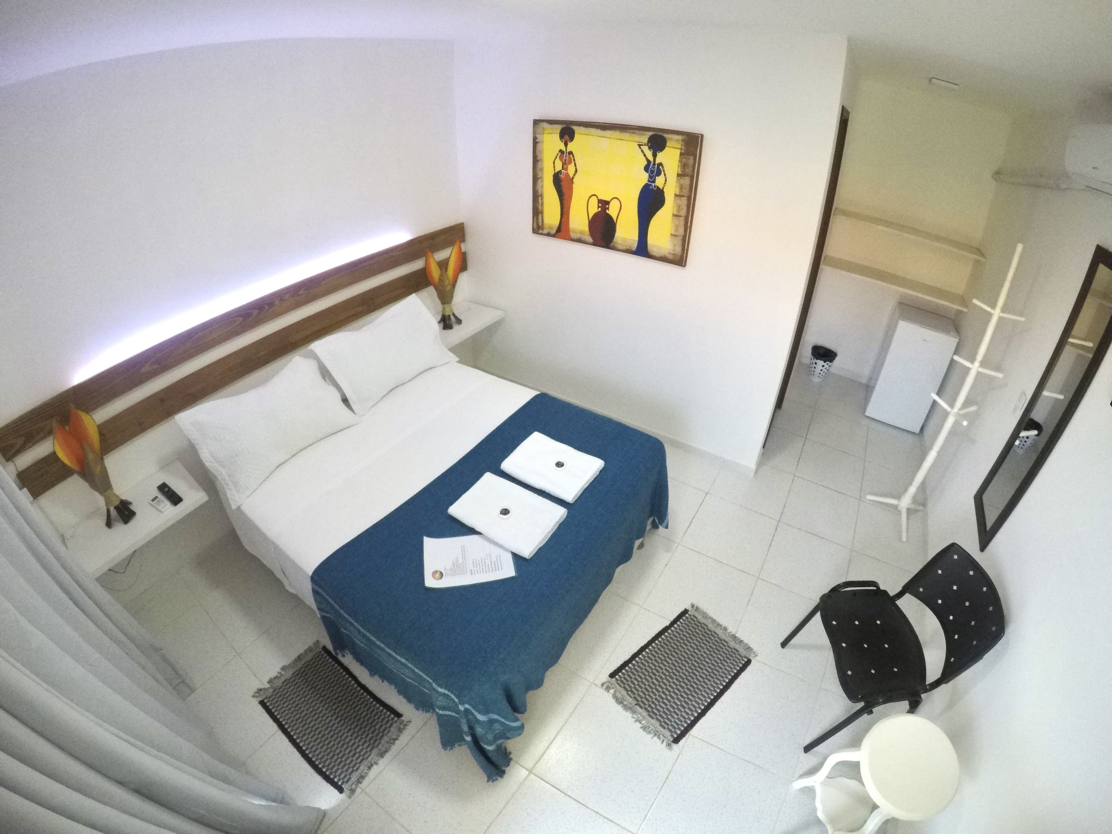 Habitación de hotel con cama, escritorio, silla, mesita, espejo y un cuadro en la pared.
