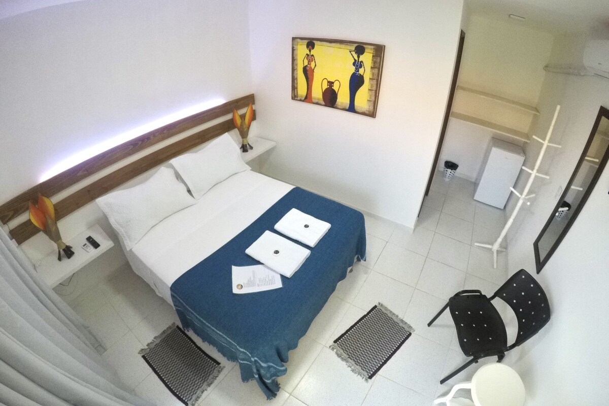 A hotel room with a bed, a desk, a chair, a small table, a mirror, and a painting on the wall.