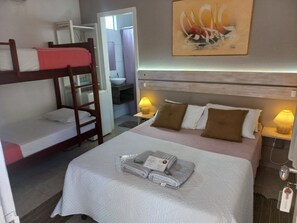 Ein Hotelzimmer mit Etagenbett, einem Einzelbett, einem Badezimmer und einem Bild an der Wand.