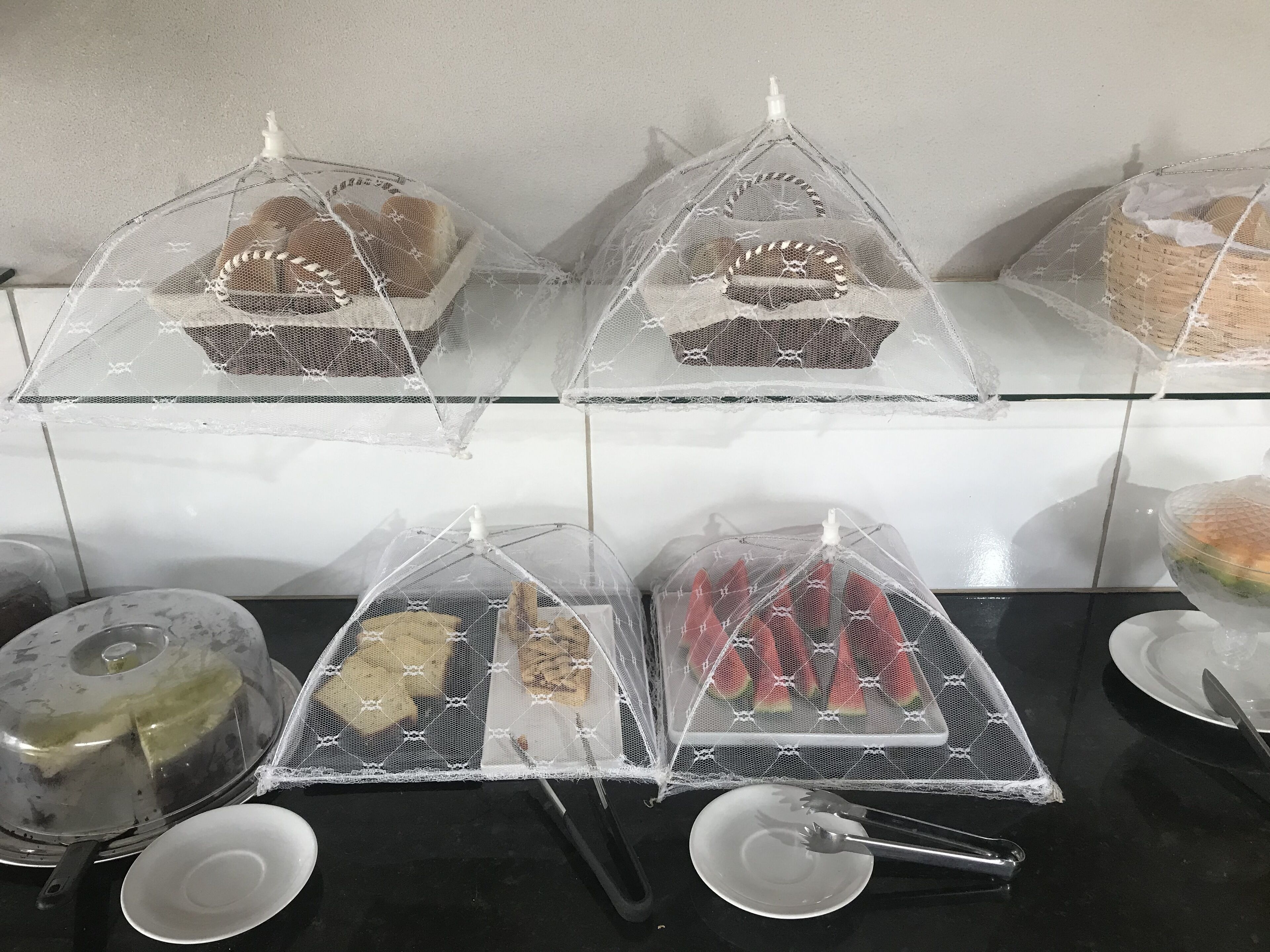 A kitchen counter with four covered food displays, a kettle, and some utensils.