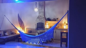 A hammock in a living area with a fireplace and a kitchen in the background. - Ayre Gostoso Pousada (São Miguel do Gostoso)