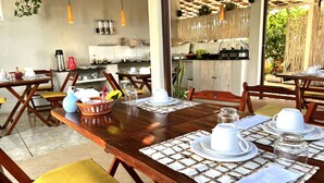 A dining area with wooden tables and chairs, a kitchen in the background, and hanging plants. - Ayre Gostoso Pousada (São Miguel do Gostoso)