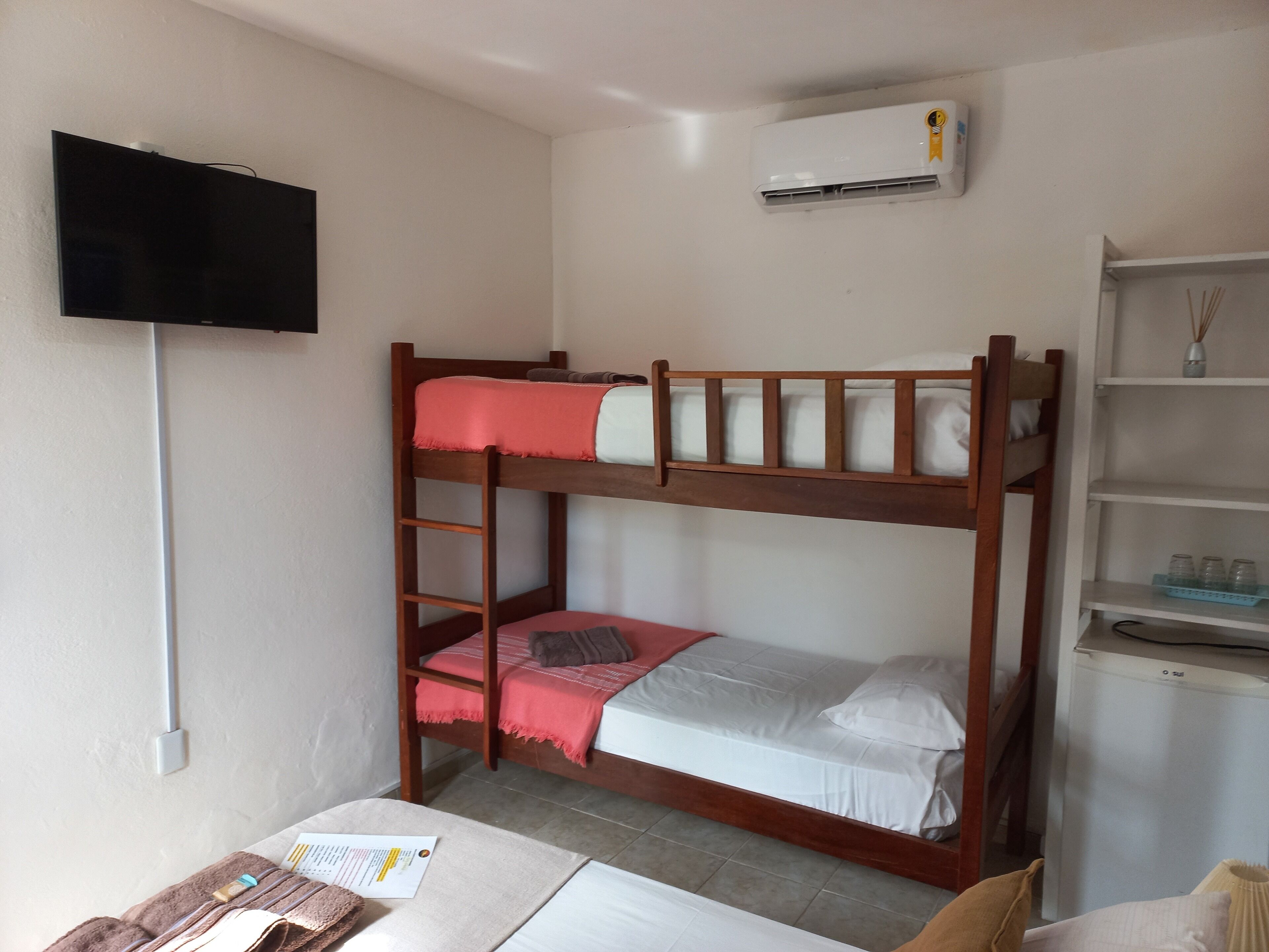 A bunk bed room with a television, air conditioning unit, and a small shelf with items.