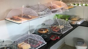 A buffet setup with various covered dishes, a clock on the wall, and a plant in the corner. - Ayre Gostoso Pousada (São Miguel do Gostoso)
