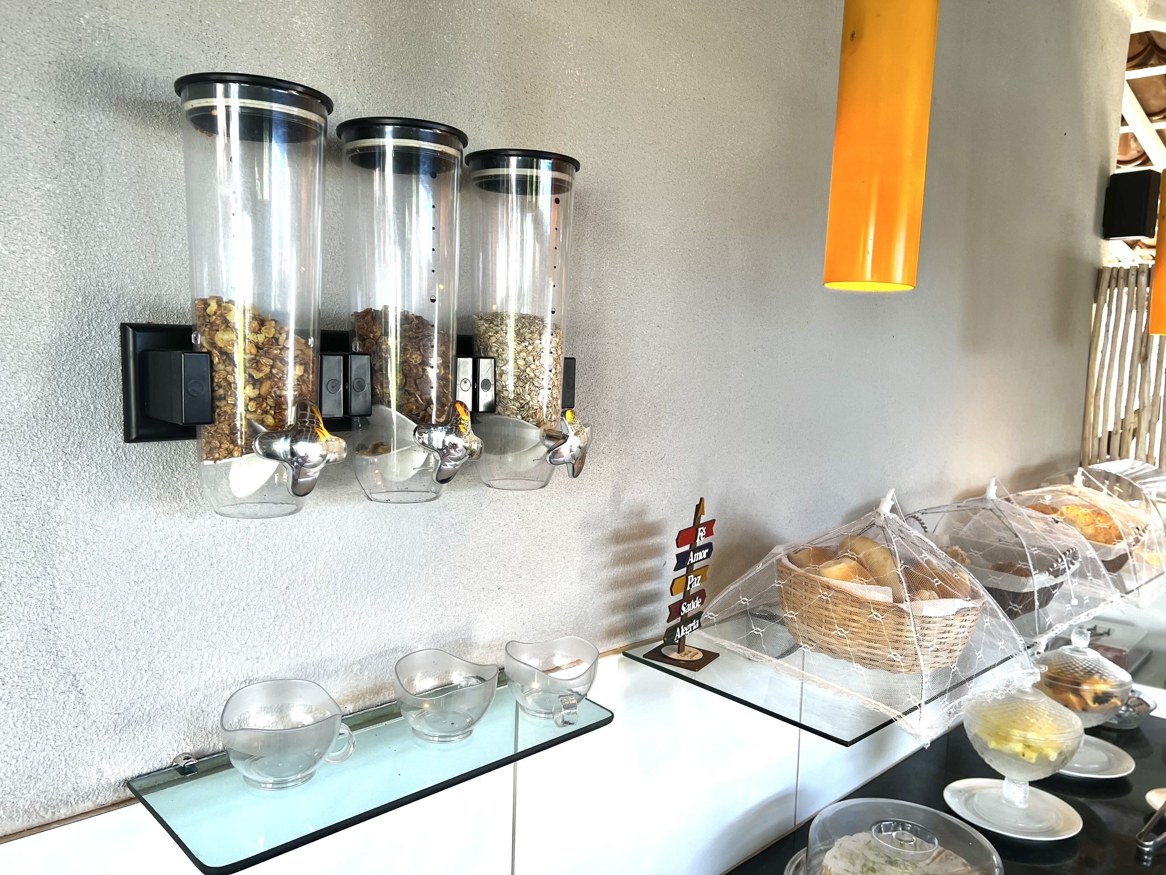 Montaje de bufé con dispensadores de vidrio transparente para los alimentos, una variedad de tazones y platos, y un expositor cubierto con productos de panadería.