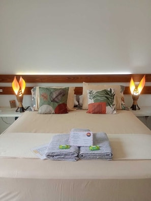 A neatly made bed with pillows, a folded towel, and a lit bedside lamp.