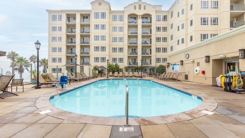 A swimming pool with lounge chairs and a building with multiple balconies in the background.