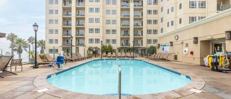 A swimming pool with lounge chairs and a building with multiple balconies in the background.
