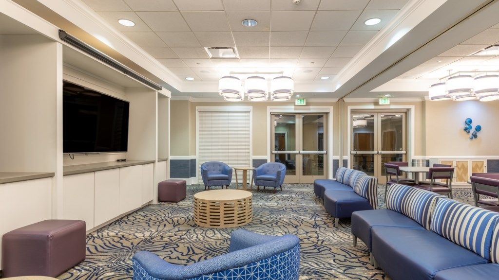 A hotel lobby with a large flat-screen TV, comfortable seating areas, and a patterned carpet.