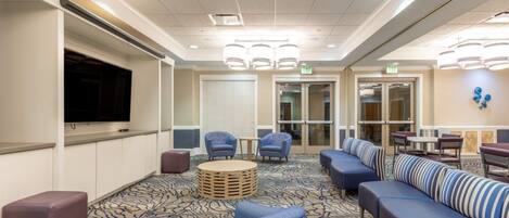 A hotel lobby with a large flat-screen TV, comfortable seating areas, and a patterned carpet.