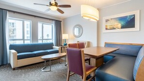 Ein Hotelzimmer mit einer Couch, einem Esstisch, einem Stuhl, einem Deckenventilator, einer Lampe, einem Spiegel und einem Bild an der Wand.