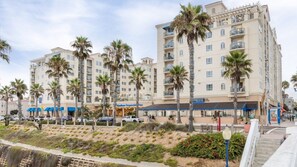Un hôtel à plusieurs étages, doté de balcons, de palmiers et donnant sur une plage.
