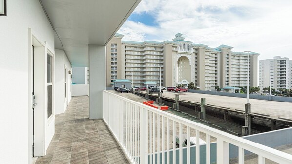 A balcony with a view of a multi-story building, a parking area with cars, and a clear sky.
