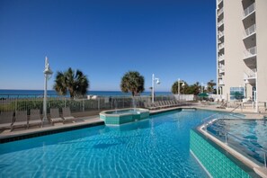 A swimming pool with a view of the ocean, surrounded by palm trees and a building with balconies.