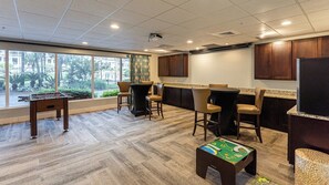 A room with a foosball table, bar area, and large windows.