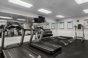 A gym with treadmills, dumbbells, and exercise posters on the wall.