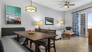 Moderni olohuone, jossa on ruokapöytä, sohva ja tuoleja, kattotuuletin sekä suuret ikkunat, joissa on verhot.
